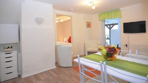 A modern, well-lit room with a dining table set for two, a television mounted on the wall, and a white wardrobe with drawers. - Apartment Oberkirchen - Ferienhaus Oberkirchen (Schmallenberg)