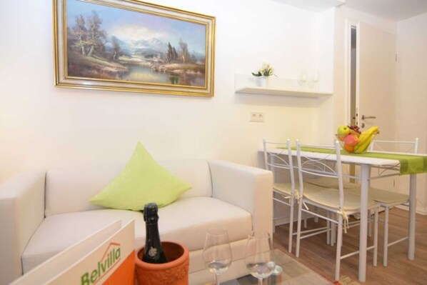 A living room with a white sofa, a green pillow, a table with wine glasses, and a painting on the wall.