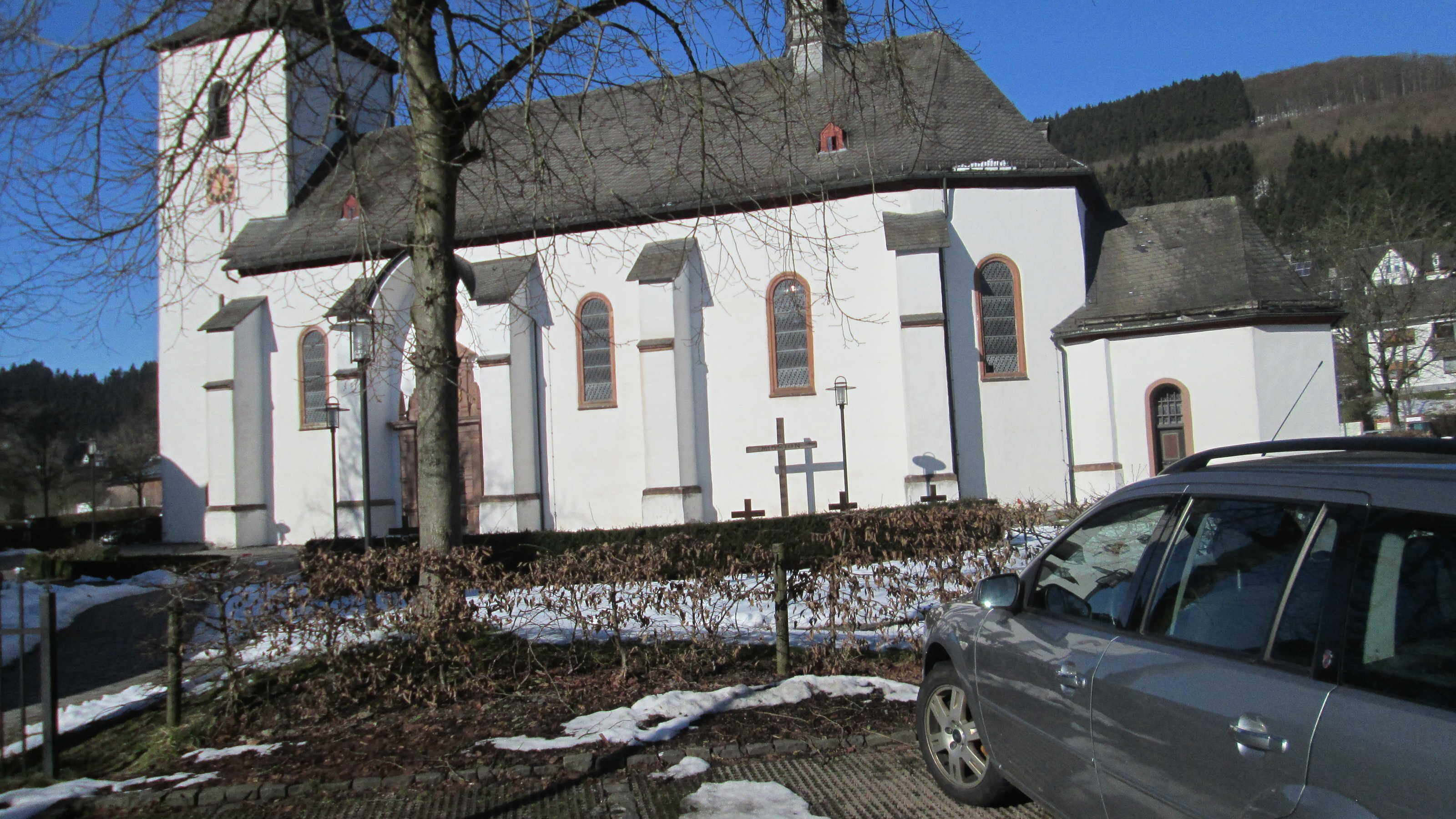 Une église blanche avec un clocher, des croix et une voiture garée devant.
