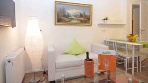 A modern living room with a white sofa, a painting on the wall, a table with a bottle and glasses, and a dining area with a table and chairs. - Apartment Oberkirchen - Ferienhaus Oberkirchen (Schmallenberg)
