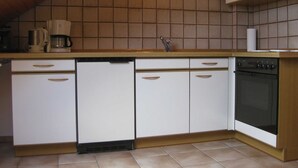 Une cuisine avec des meubles blancs, un lave-vaisselle, une machine à café et un four.