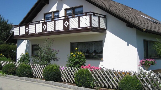 Une maison à deux étages avec un balcon, des murs extérieurs blancs et un toit marron.