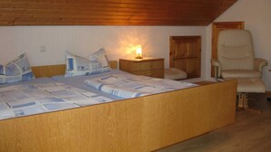 Une chambre avec un plafond en bois, un lit avec une literie à motifs, une table de chevet avec une lampe et une chaise.