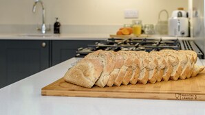 Une miche de pain sur une planche à découper en bois, dans une cuisine au design moderne, avec une cuisinière à gaz et un four à micro-ondes en arrière-plan.