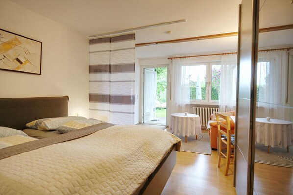 A bedroom with a bed, a chair, a table, and a view of the outdoors.