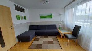 Una sala de estar moderna con un sofá modular, un sillón, una mesita y un ventanal con cortinas traslúcidas.