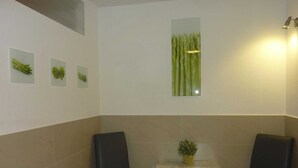 Un comedor con una mesa cubierta por un mantel estampado, dos sillas negras y una planta en maceta sobre la mesa.