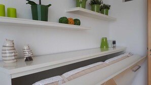 Habitación de hotel con estantes blancos que exhiben adornos, una cama con colchón blanco y una puerta a la derecha.