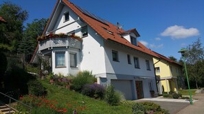 A two-story house with a red-tiled roof, white walls, and a small balcony with flower boxes.