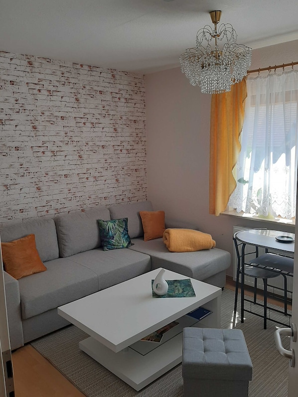 A modern living room with a grey sofa, a white coffee table, and a dining area with a small table and chairs.
