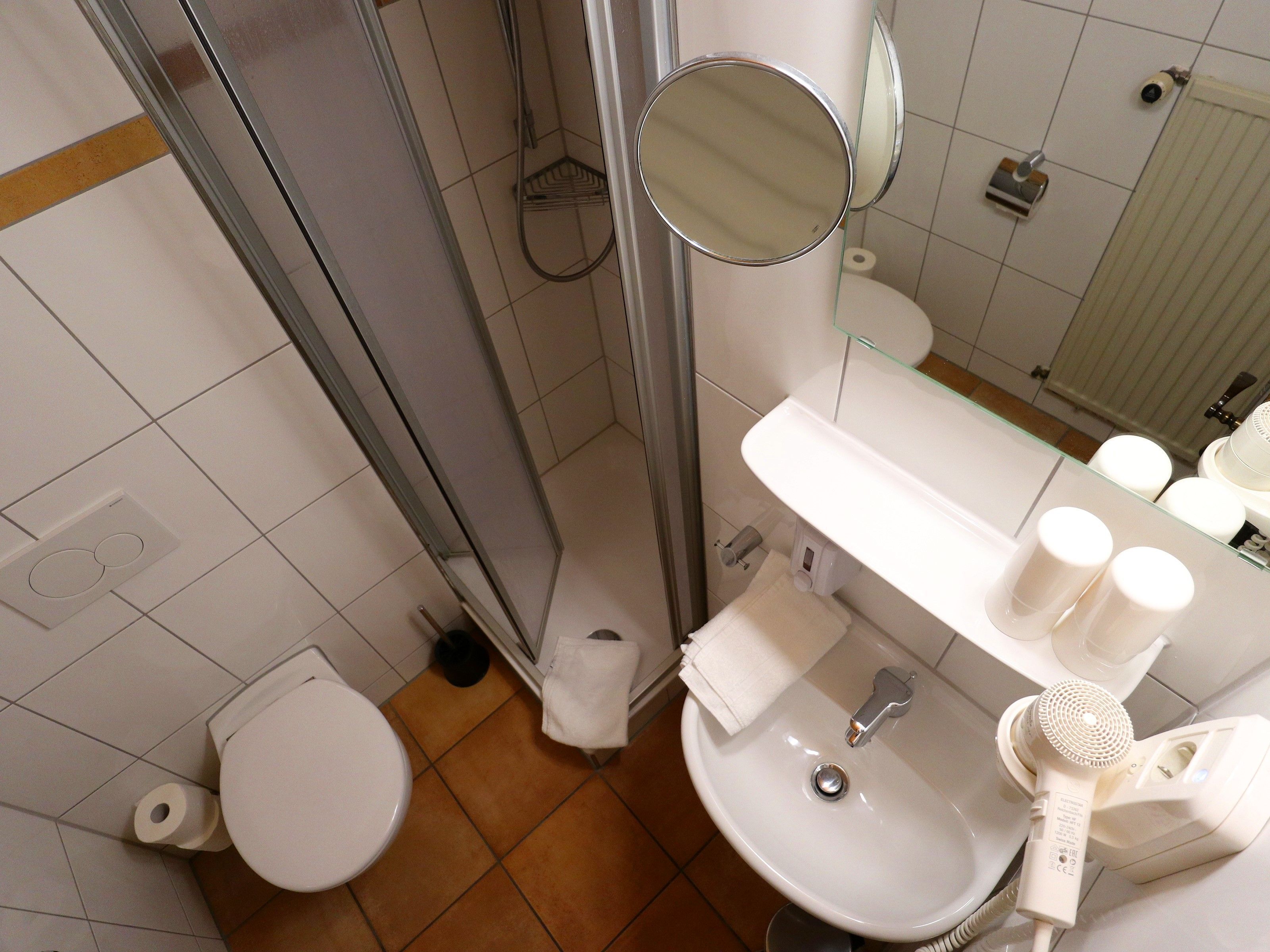 Ein Badezimmer mit Toilette, Waschbecken, Spiegel, Dusche und Handtuchhalter.
