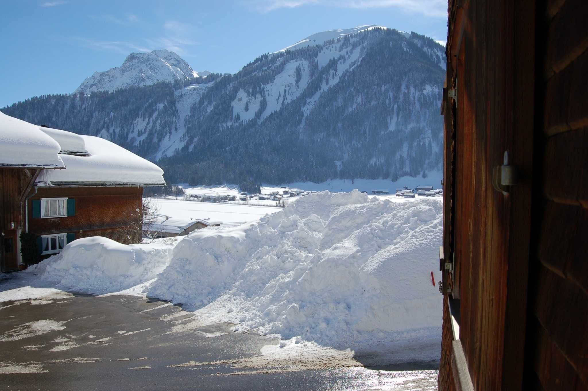 A snowy mountain landscape with a wooden building and a pile of snow in the foreground.
