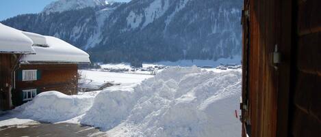 A snowy mountain landscape with a wooden building and a pile of snow in the foreground.