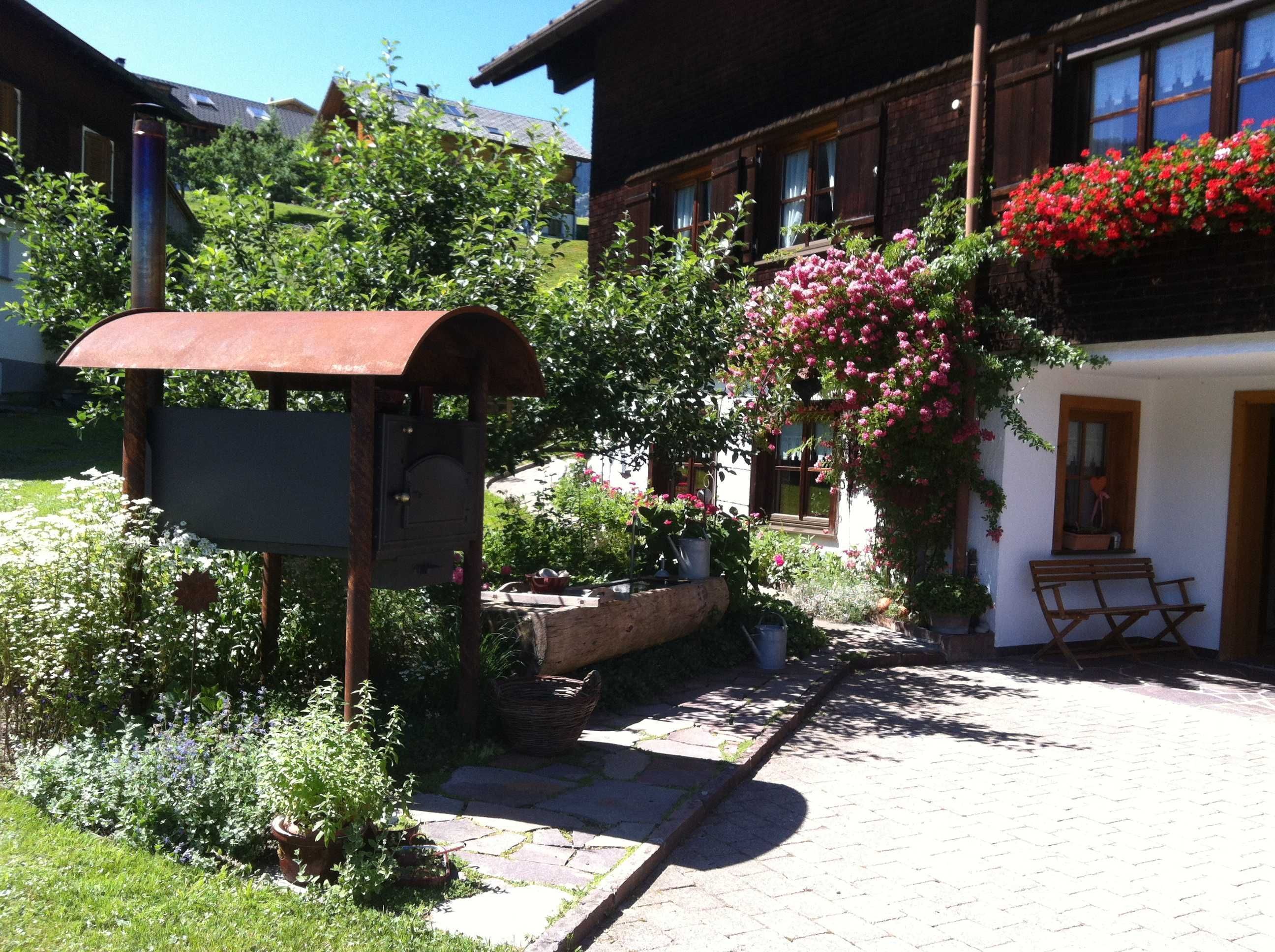 A rustic building with a garden area, a wooden bench, and a mailbox.