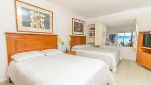 Quarto de hotel com duas camas, uma cabeceira de madeira, uma mesa de cabeceira com um vaso e um espelho grande.
