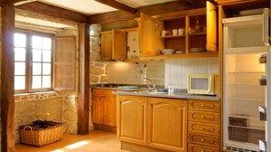 A kitchen with wooden cabinets, a stone wall, and a built-in microwave. - Zen Vouga - Quinta do Fundo de Vila (Oliveira de Frades)