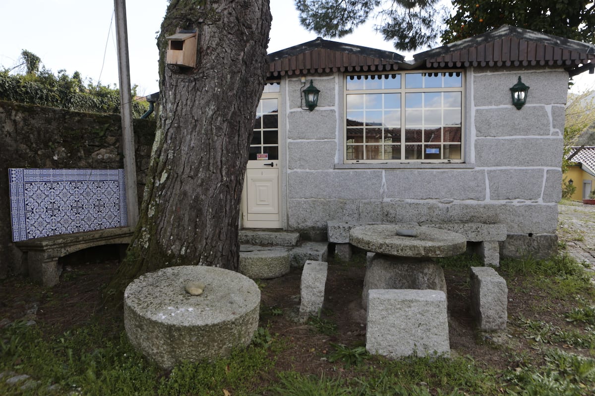 Ein Steinhaus mit gefliestem Eingangsbereich, einem hölzernen Vogelhaus und einem kleinen Tisch auf Steinsockel.