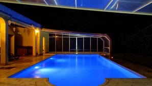 An indoor swimming pool with a blue-lit edge, surrounded by a covered patio area with seating. - Zen Vouga - Quinta do Fundo de Vila (Oliveira de Frades)