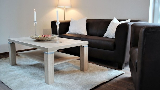 Un salon moderne avec une table basse en bois, un canapé marron foncé et un tapis blanc.