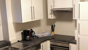 Une cuisine compacte avec des meubles blancs, un évier en acier inoxydable, une machine à café et une cuisinière.