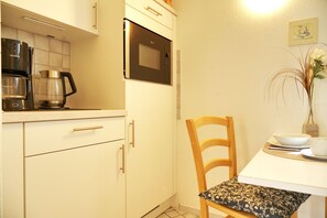 A compact kitchen with a coffee maker, microwave, and a dining area with a chair and table. - Holiday Oasis - Apartment No. 2 - Holiday oasis (Bad Dürrheim)