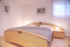 A bedroom with a wooden bed, a bedside table with a lamp, and two framed pictures on the wall. - Holiday Oasis - Apartment No. 2 - Holiday oasis (Bad Dürrheim)