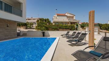 A swimming pool with lounge chairs, a stone wall, and a building in the background.
