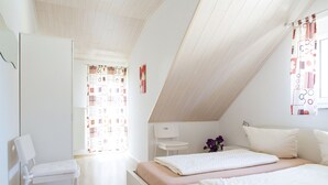 Una camera da letto moderna con soffitto a falde, un letto con due cuscini, una sedia e un tavolino con un vaso di fiori.