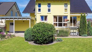 Una casa gialla a due piani con tetto scuro, un portico coperto e un giardino curato.