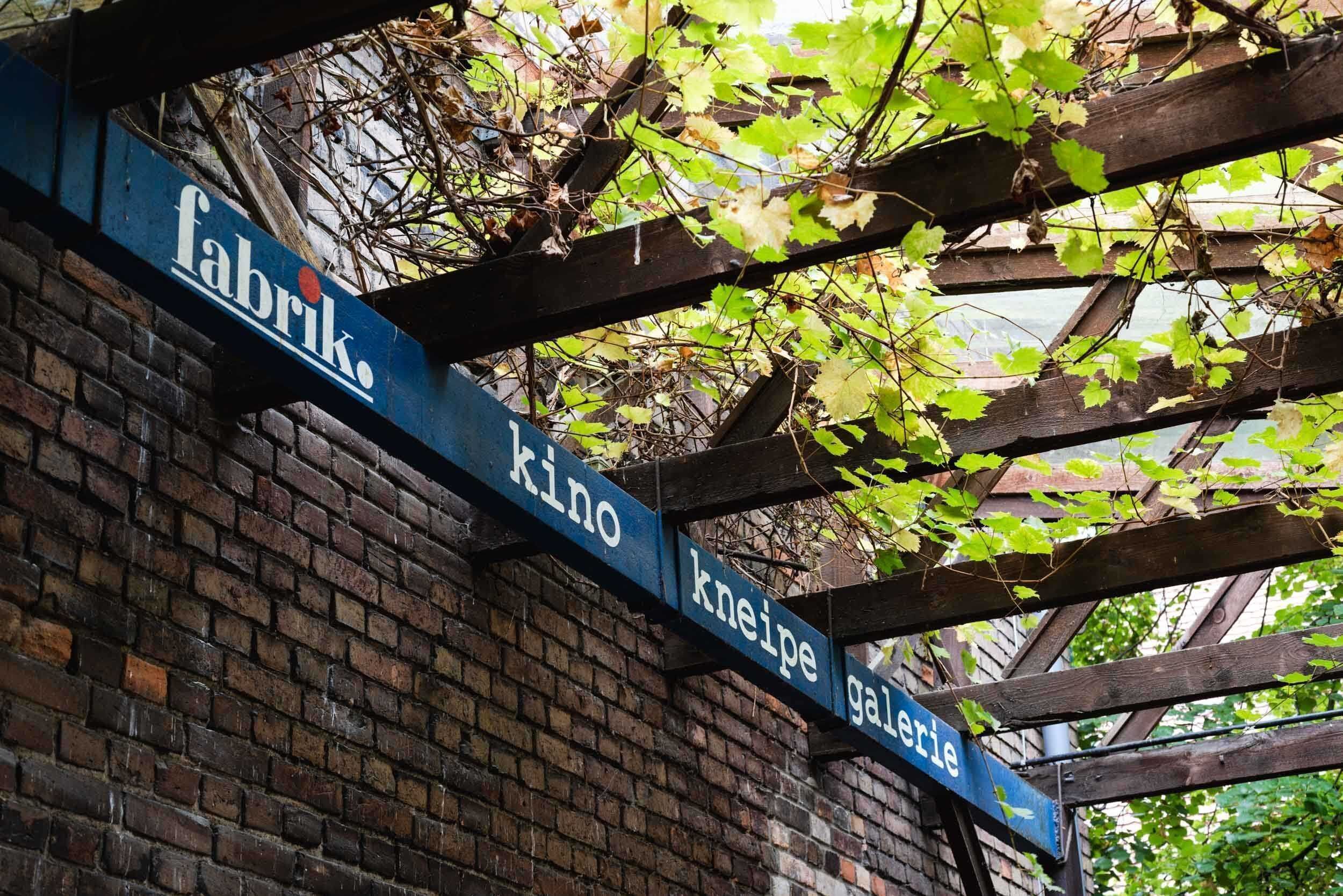 Ein Schild mit den Aufschriften 'Fabrik', 'Kino', 'Kneipe' und 'Galerie' an einer Holzkonstruktion.