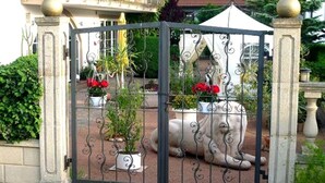 A gated entrance with a decorative iron gate, a stone pillar, and a potted plant with red flowers.