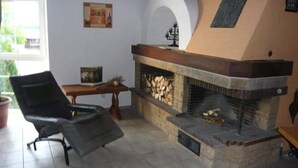 A living room with a fireplace, a black leather chair, a wooden table, and a window.