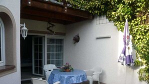 An outdoor patio with a round table, two chairs, a potted plant, and a flag.