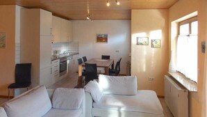 Un espacio habitable compacto con kitchenette, zona de comedor y área de estar con sofá y mesa de centro.