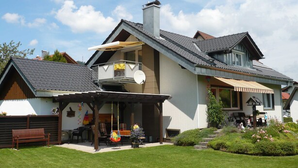 Une maison moderne dotée d’un balcon, d’une terrasse couverte et d’un jardin.