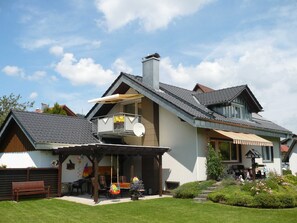 Une maison moderne dotée d’un balcon, d’une terrasse couverte et d’un jardin.