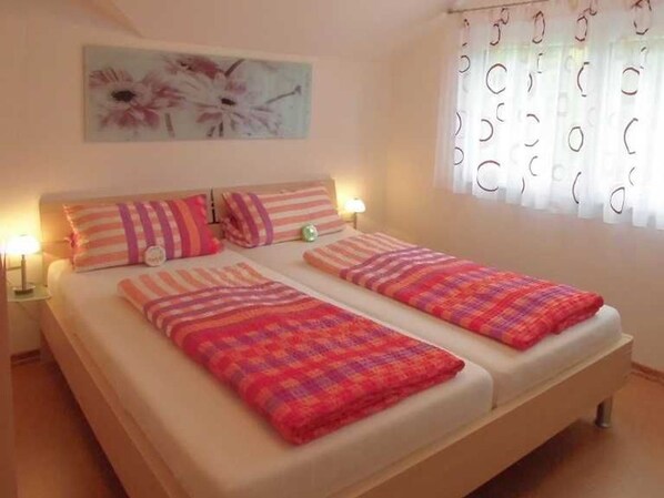 Un lit double avec une literie à rayures, une table de chevet avec une lampe et une fenêtre ornée de rideaux à motifs circulaires.