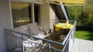 Un balcon doté d’une marquise jaune, de deux chaises, d’une table recouverte d’une nappe jaune et d’une porte vitrée donnant sur un espace intérieur.