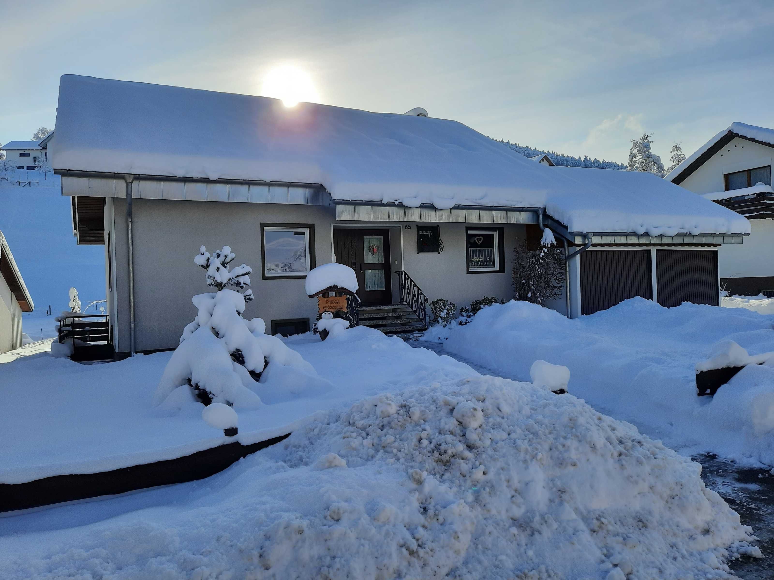 A house with a snow-covered roof and driveway, a mailbox, and a small garden area.
