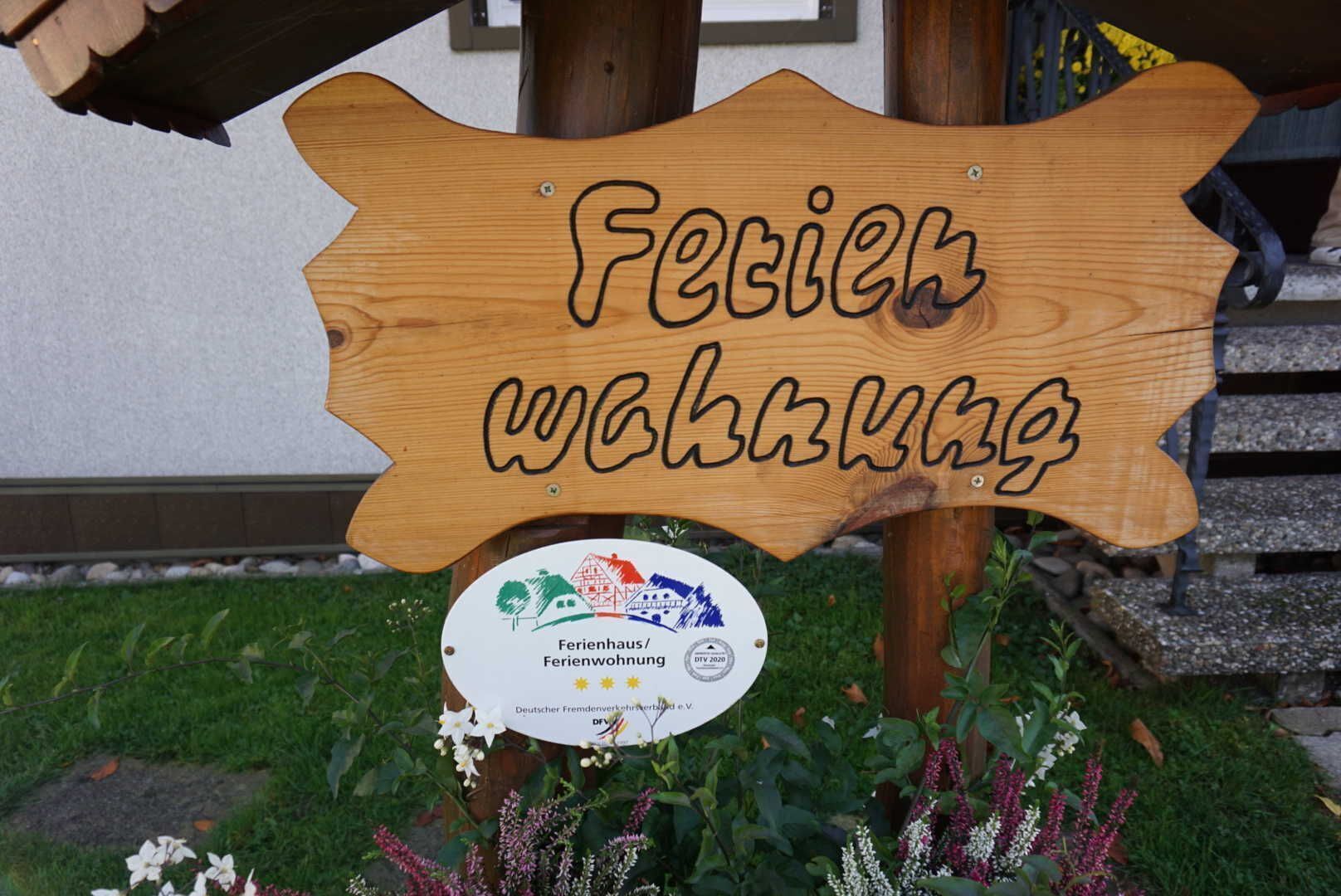 Ein Holzschild mit dem Schriftzug 'Ferienwohnung' und einem Aufkleber darunter.