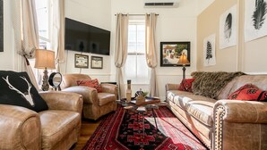 A living room with leather sofas, a patterned rug, and wall art. - In Town Villas | Luxury On Main St. | Hot Tub (Fredericksburg)