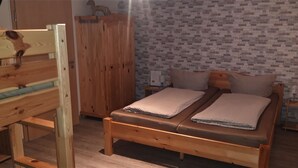 A wooden bed with a headboard, a wardrobe, and a brick-patterned wall. - Four-bed room - Gästehaus Claudia (Rust)