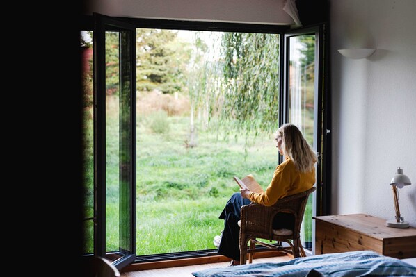A person reading a book in a room with a large sliding glass door leading to a garden.