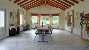 A spacious dining area with a long table, wooden beams, large windows, and a view of greenery outside. - Double room blue - Winery Baumer (Vogtsburg im Kaiserstuhl)