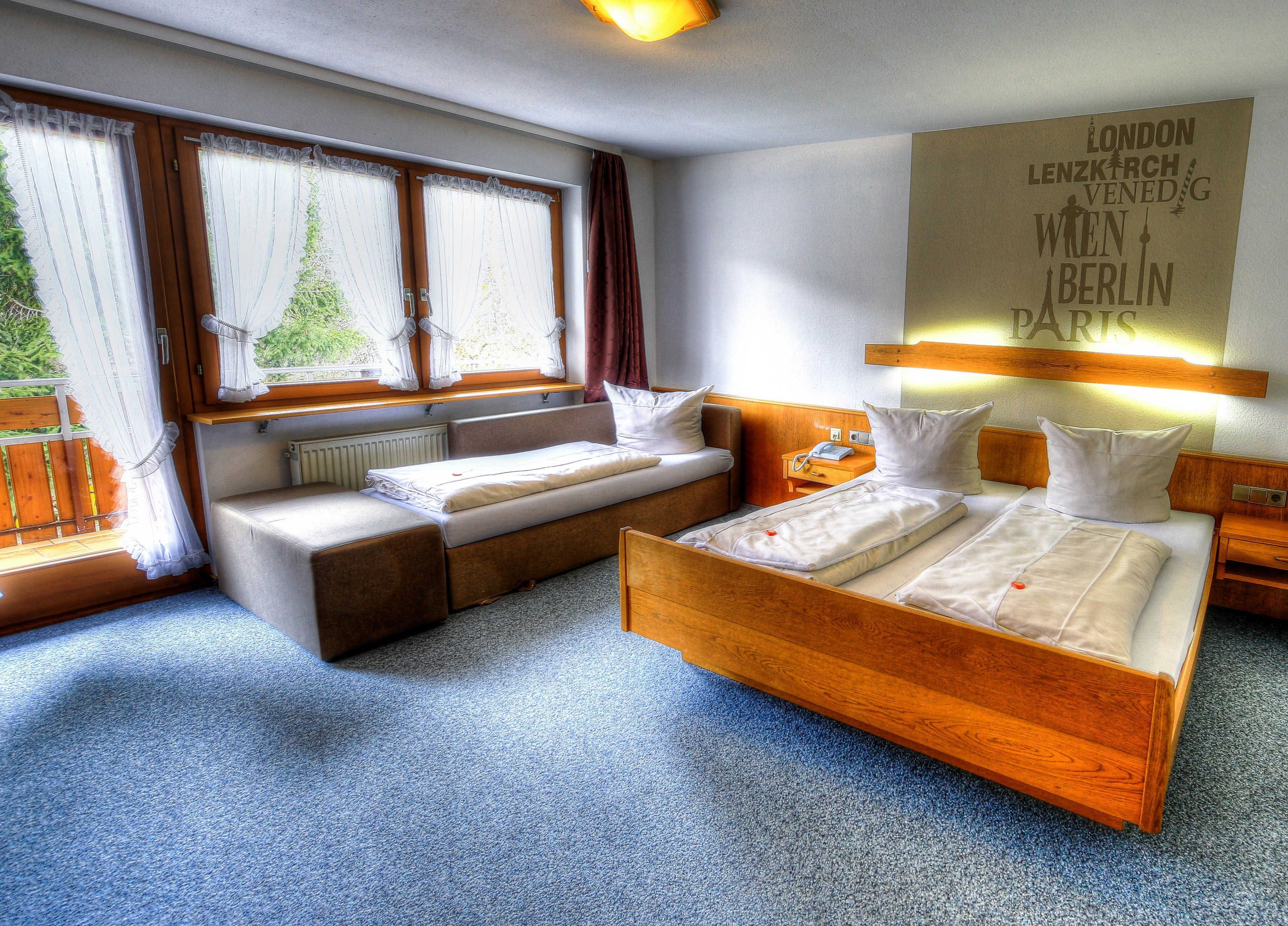 Une chambre d’hôtel comprenant un lit, un canapé-lit, une table de chevet, une lampe et une fenêtre avec des rideaux.