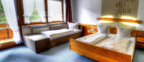 Une chambre d’hôtel comprenant un lit, un canapé-lit, une table de chevet, une lampe et une fenêtre avec des rideaux.