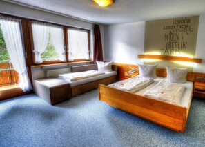 Une chambre d’hôtel comprenant un lit, un canapé-lit, une table de chevet, une lampe et une fenêtre avec des rideaux.