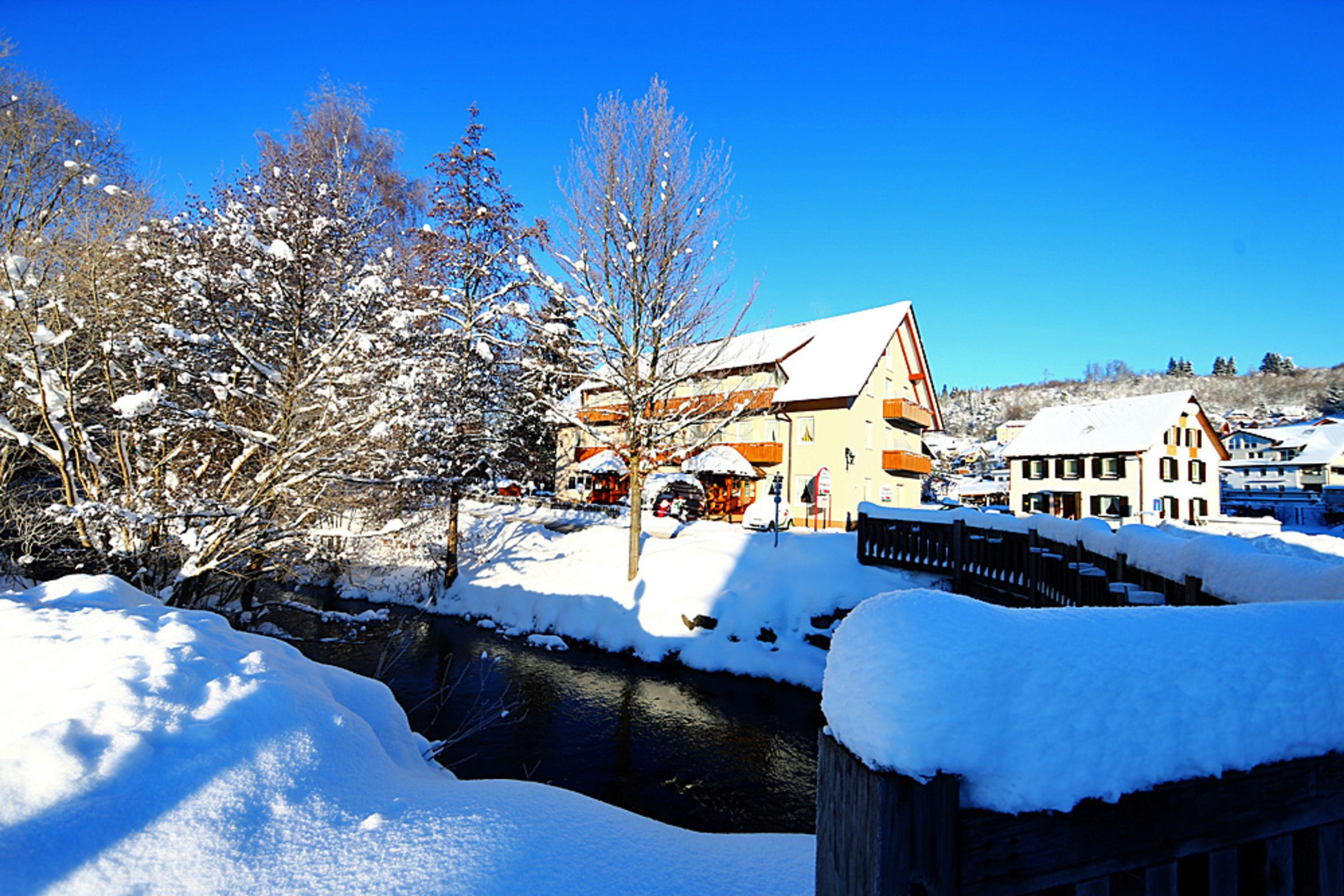 Een besneeuwde stad met gebouwen, een rivier en kale bomen.