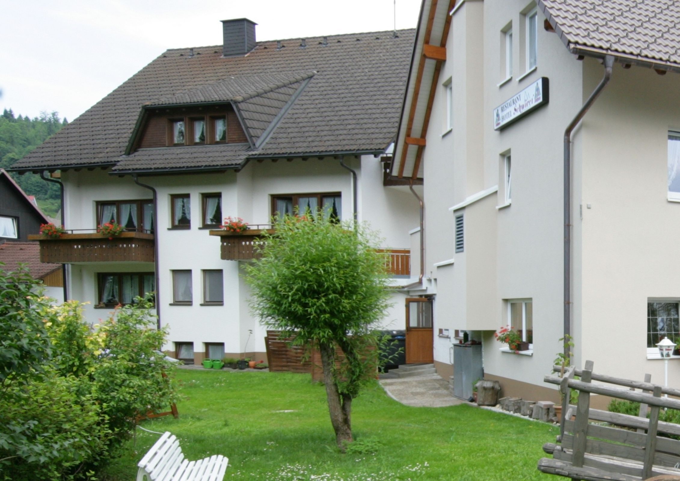 A two-story building with a balcony, a small garden, and a wooden fence.