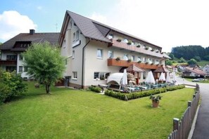 Un hôtel à plusieurs étages, doté d’un toit plat, de balcons ornés de plantes et d’une pelouse bien entretenue.